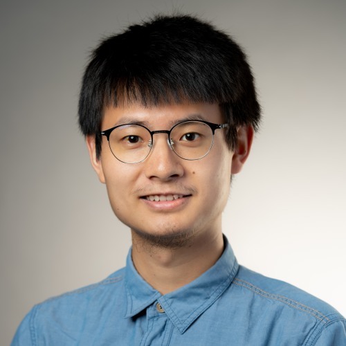 Xinyu Dai smiling in front of a gray background.