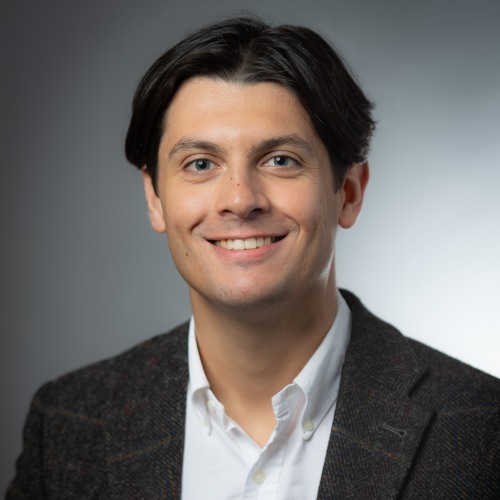 Adrien Foutelet smiling in front of a gray background.