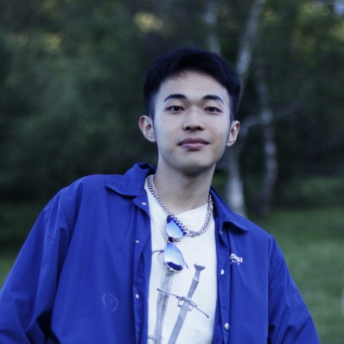 Zachk Huang smiling and posing in front of park greenery.