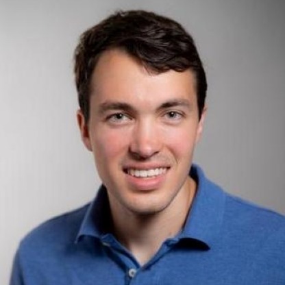 Michael Neubauer smiling in front of a gray background.