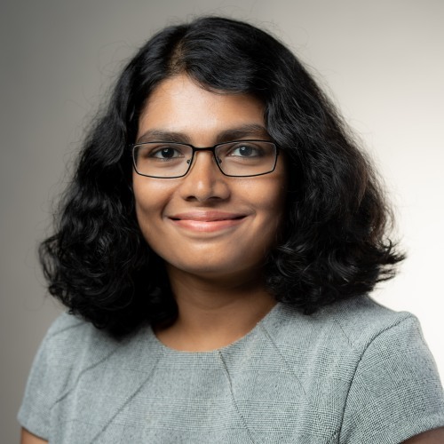 Sai Pitre smiling in front of a gray background