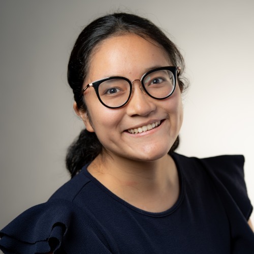 Raquel Badillo Salas smiling in front of a gray background.