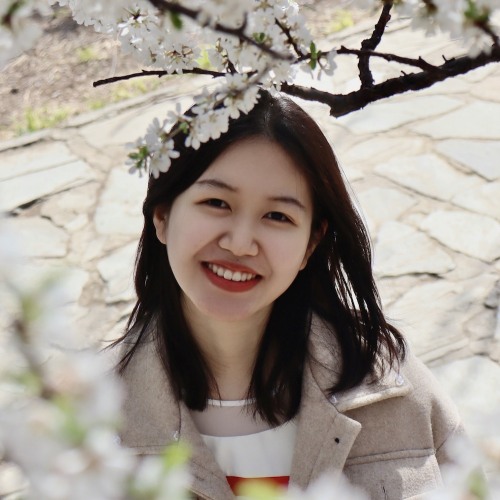 Yulin Yang smiling under tree blossoms.