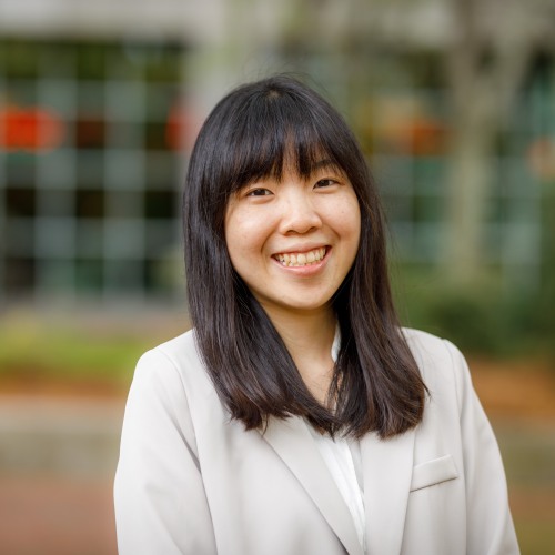 Photo of Nora Lu wearing white blouse against an outdoor greenery background