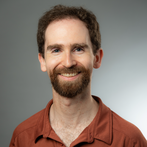 Photo of Leo Zucker wearing rust colored collared shirt against gray background