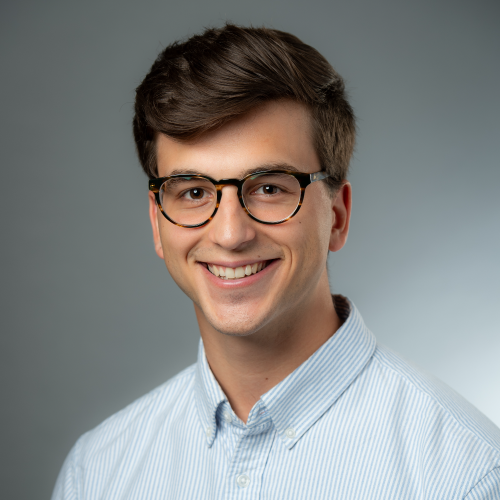 Photo of Brendan Chapuis with short brown hair, wearing glasses and a light blue collared shirt