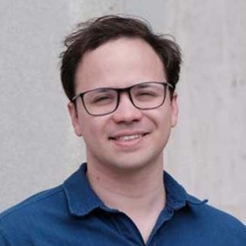 Photo of Derek Baum, who is a white male with short brown hair and glasses, wearing a blue button-down shirt against a gray backdrop