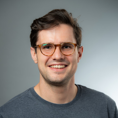 Sean McCulloch who has short brown hair, wears round red-framed eyeglasses, and is wearing a gray tee shirt