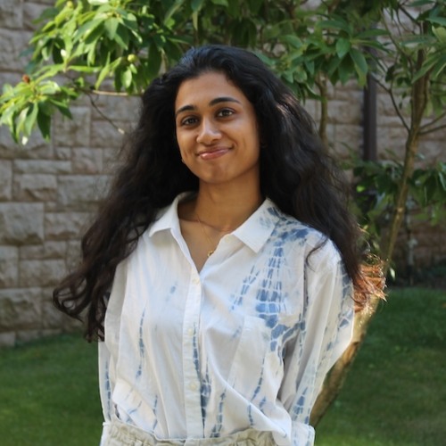 Chandni Shyam wearing white blouse in front of brick building and greenery