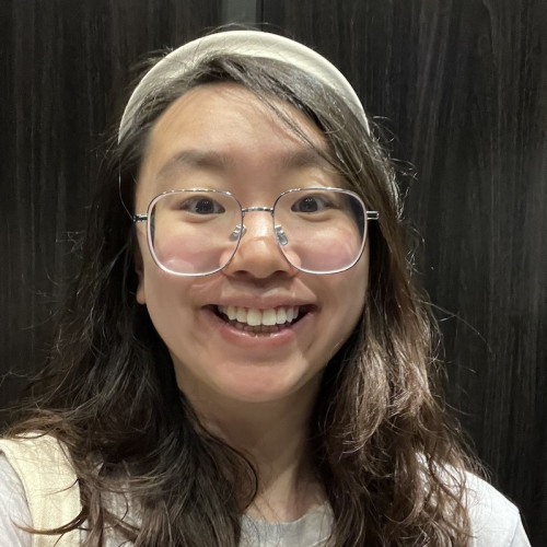 Eliza Ge wearing white sweater and white headband against dark background